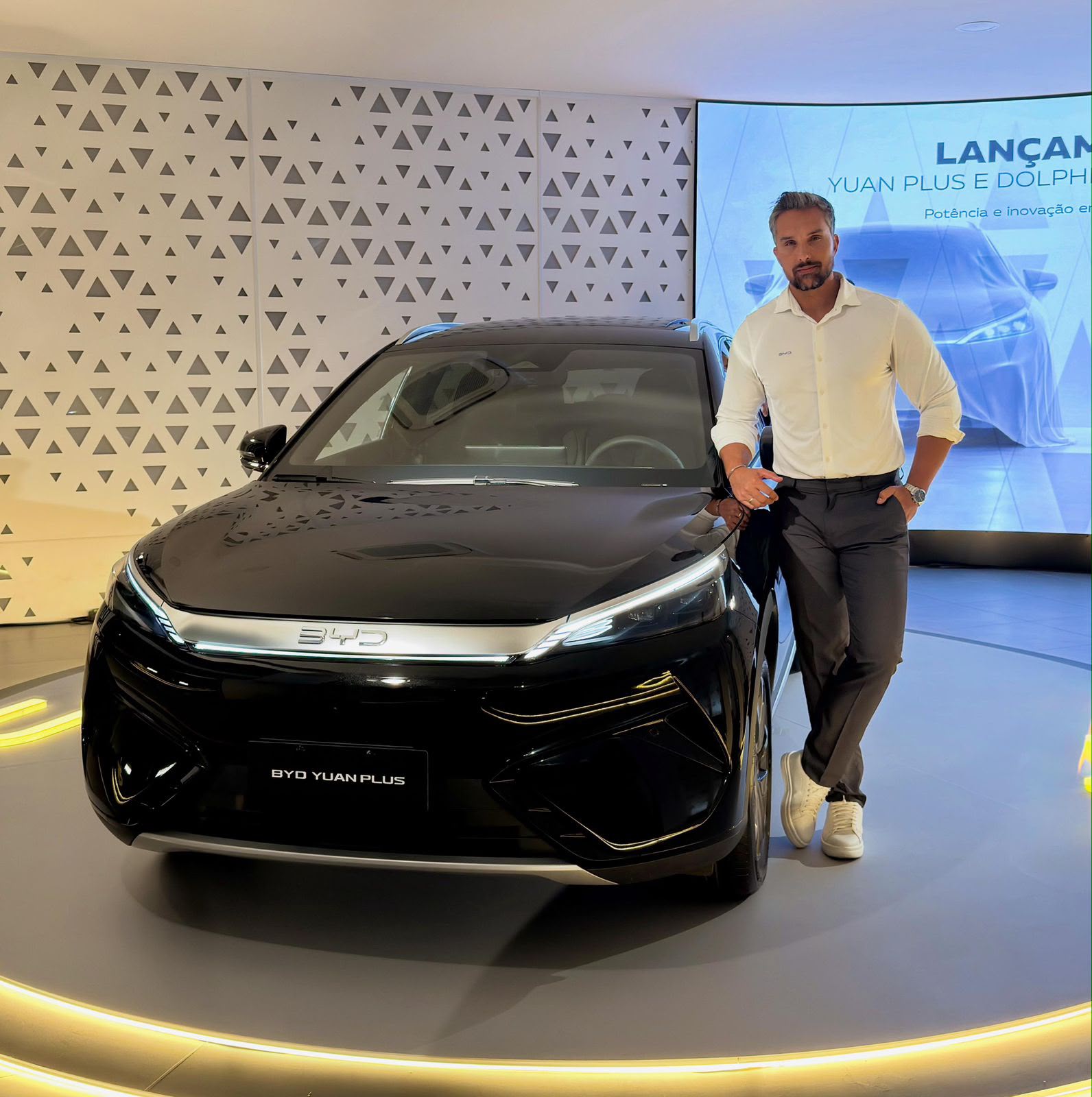 Modelo comercial da agência Tariju Eventos posando para campanha publicitária ao lado de carro BYD